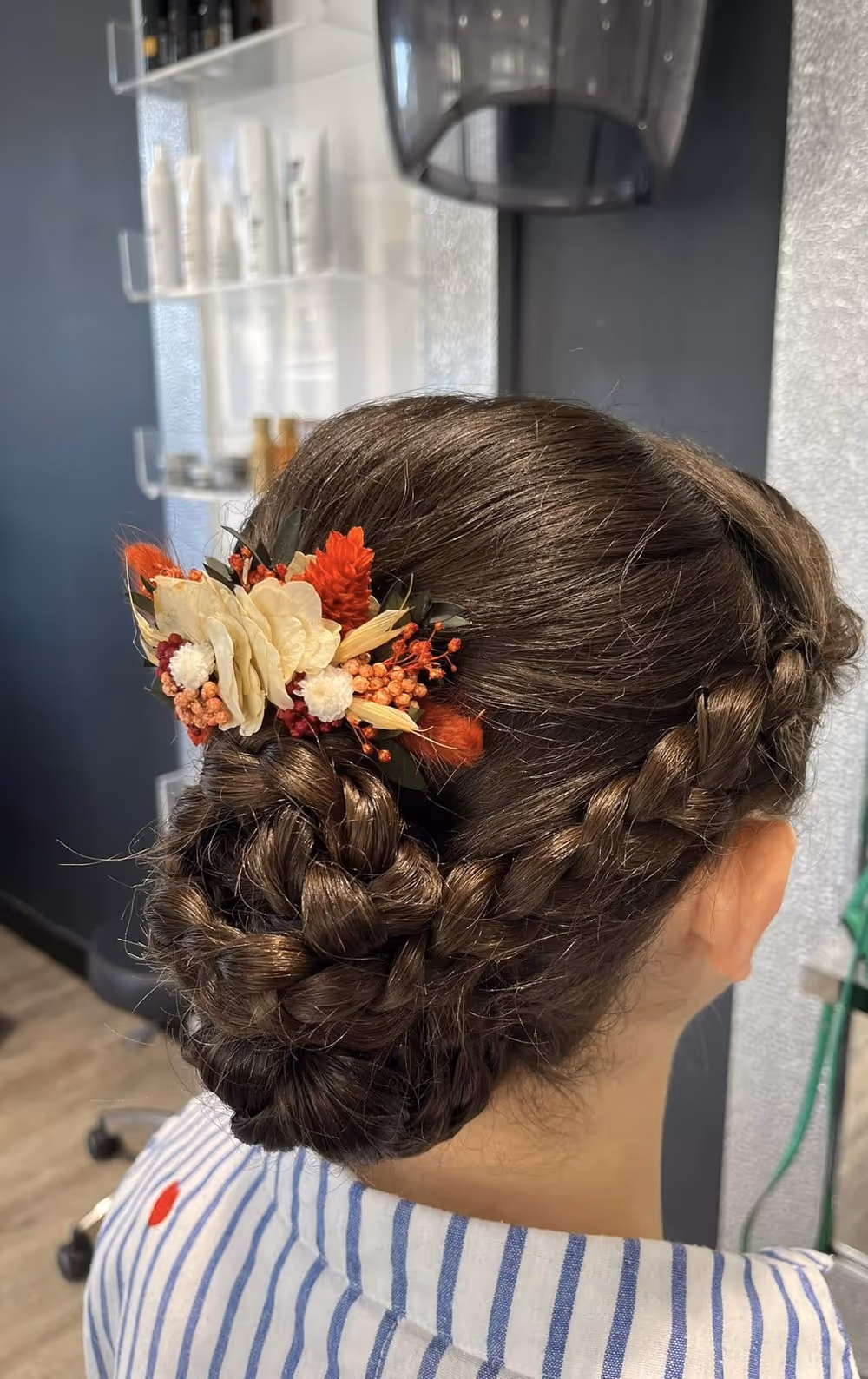Chignon tressé bas orné de fleurs séchées orangées et crème